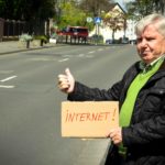 Ein älterer Mann steht an der Straße und hält ein Schild hoch, auf dem "Internet" steht.